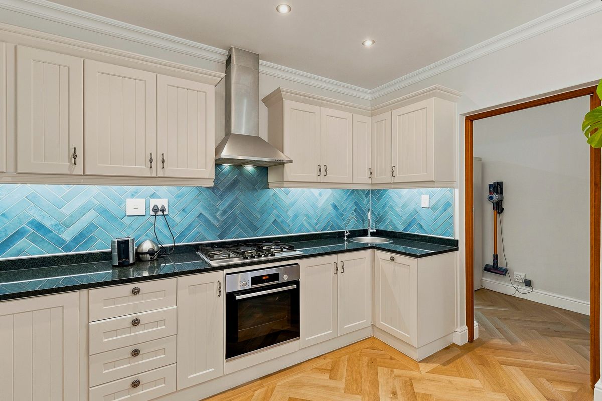 Modern kitchen featuring shaker-style cabinetry, striking blue herringbone tile backsplash, granite countertops, and high-quality built-in appliances with elegant herringbone timber flooring.