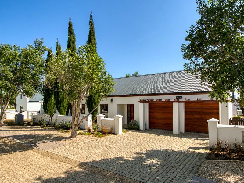 A well-maintained front exterior featuring a paved driveway, double garage with wooden doors, and a modern corrugated metal roof.