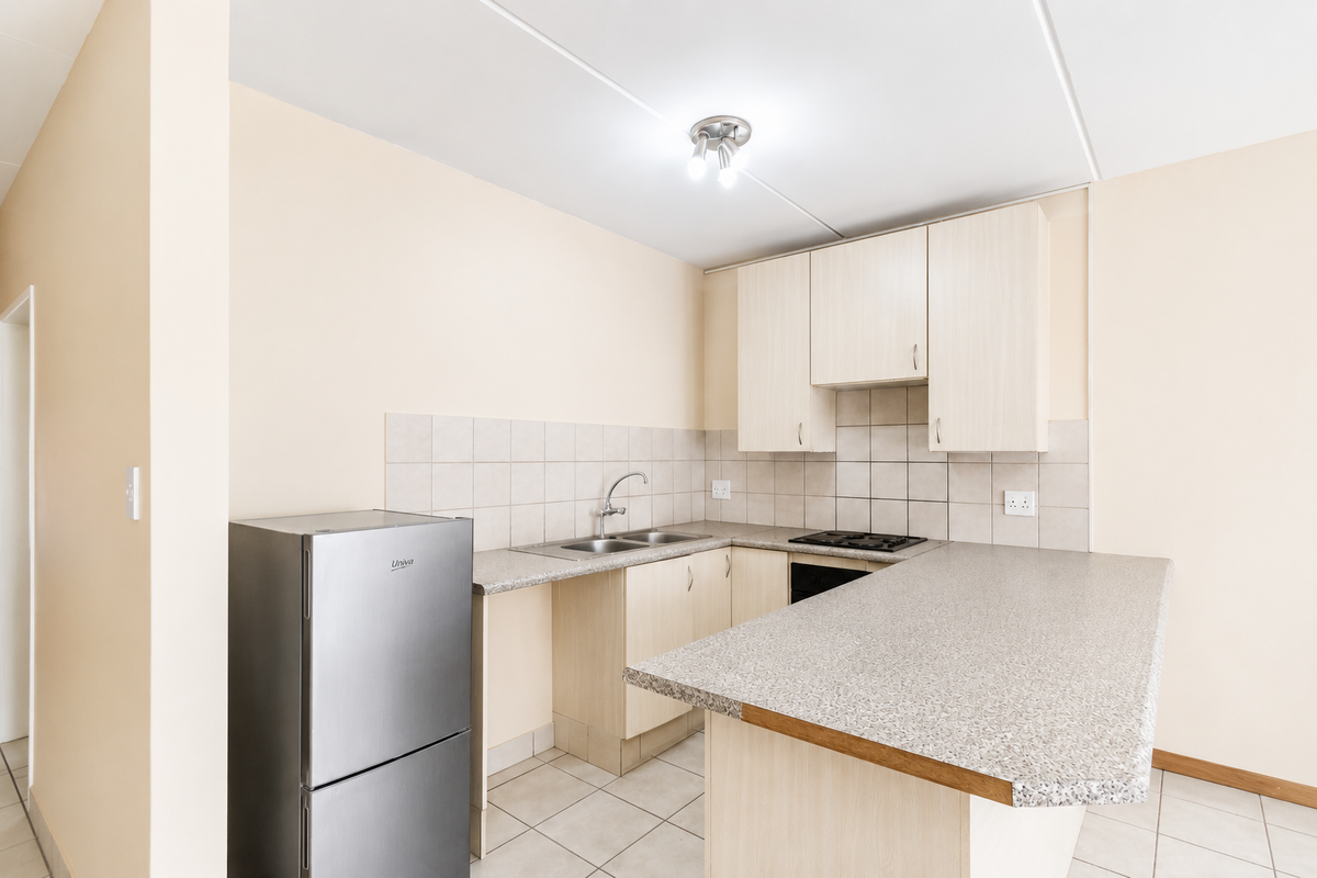A functional kitchen featuring light wood-look cabinetry, laminate countertops, a double sink, and built-in cooking appliances with neutral ceramic tiling.