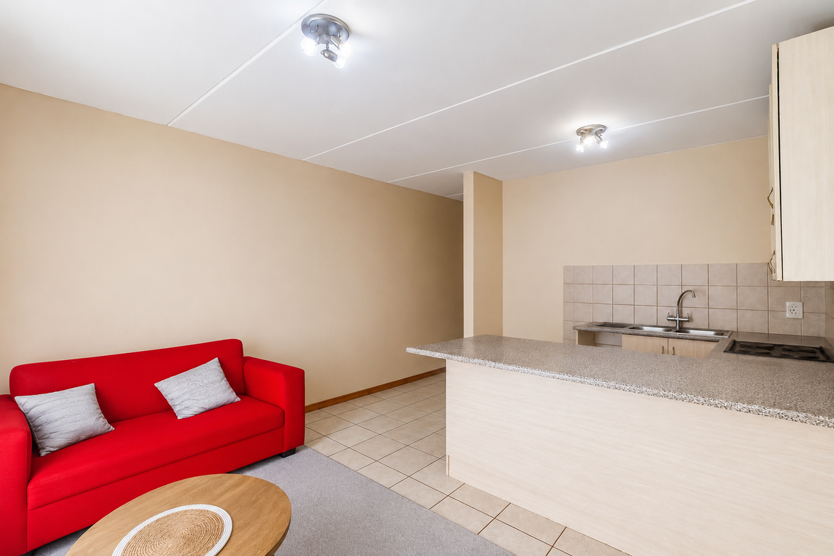 Open plan living area featuring a compact kitchen with laminate countertops, built-in hob, and tiled backsplash, seamlessly connected to the lounge space.