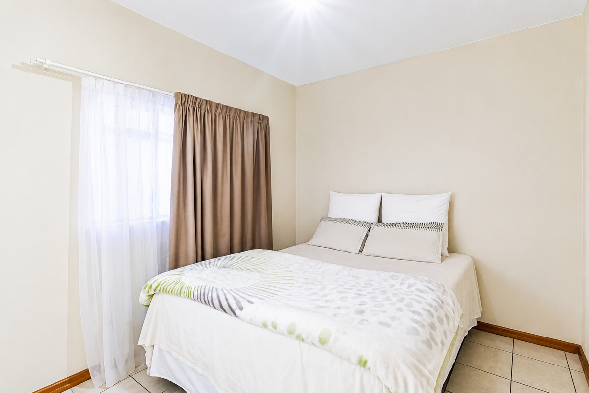A simple bedroom featuring neutral wall tones, tiled flooring, and a window fitted with a curtain rod.