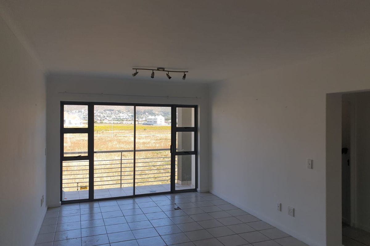 An empty, open-plan living area featuring tiled flooring, track lighting, and large sliding glass doors leading to a balcony with scenic views.