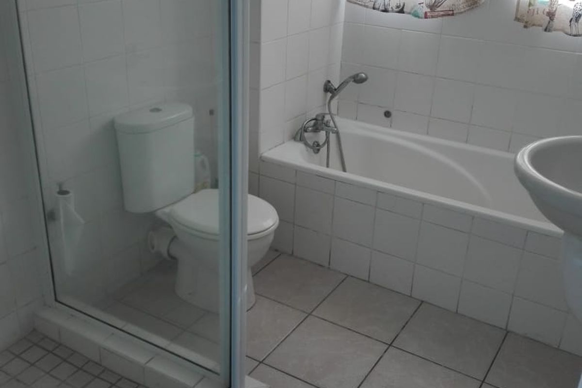 A functional bathroom featuring a shower enclosure, bathtub, pedestal basin, and tiled finishes throughout.