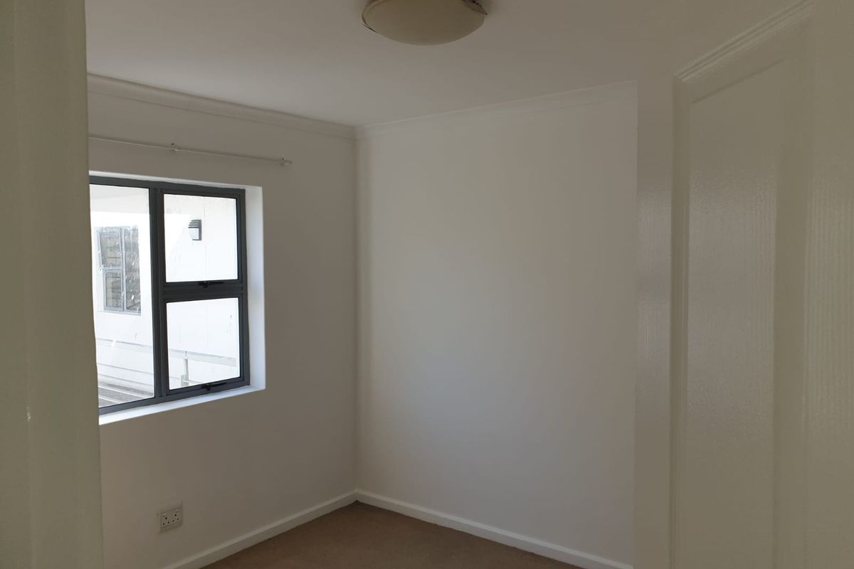 A clean, empty bedroom featuring neutral walls, carpet flooring, and an aluminium-framed window, providing a blank canvas for personalization.