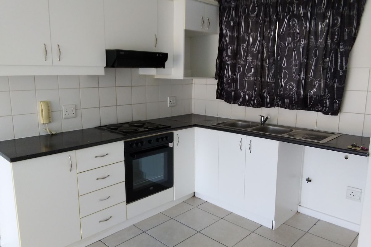 A functional kitchen featuring white cabinetry, dark countertops, a built-in oven and hob, and tiled flooring with a tiled backsplash.