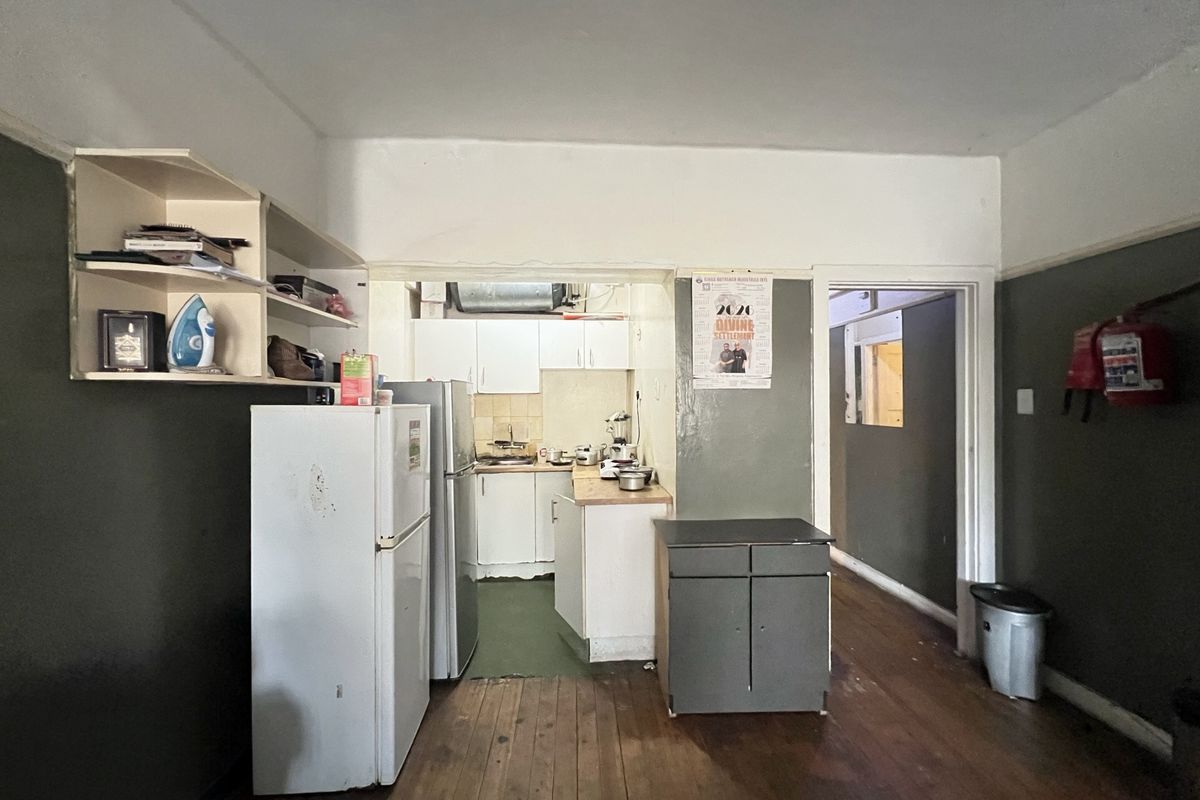 Open plan living area featuring timber flooring and a compact kitchen with built-in cabinetry and sink, requiring cosmetic updates.