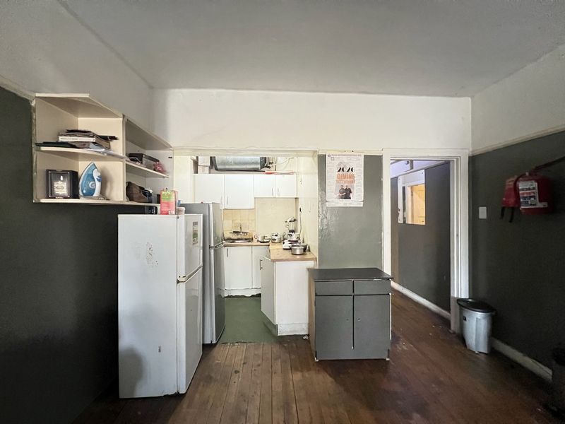 Open plan living area featuring timber flooring and a compact kitchen with built-in cabinetry and sink, requiring cosmetic updates.