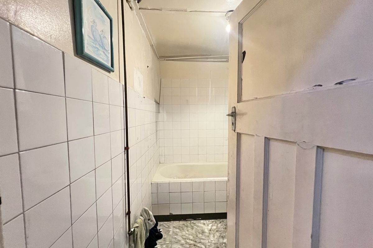 A dated bathroom featuring a built-in bathtub, tiled walls, and tiled flooring, requiring renovation to update the finishes and address structural wear.