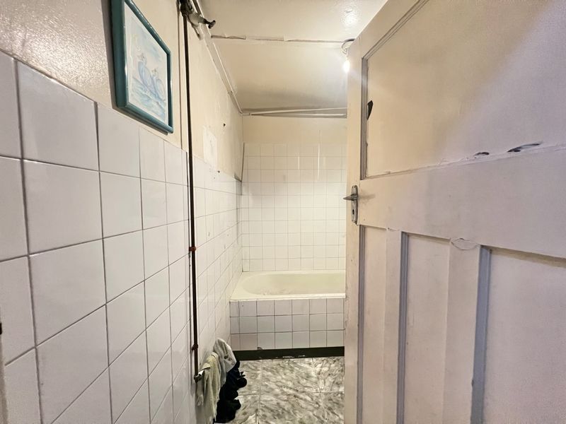 A dated bathroom featuring a built-in bathtub, tiled walls, and tiled flooring, requiring renovation to update the finishes and address structural wear.