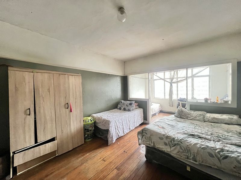 Spacious bedroom featuring original hardwood flooring, large windows providing natural light, and a classic picture rail, offering potential for modernization and cosmetic updates.
