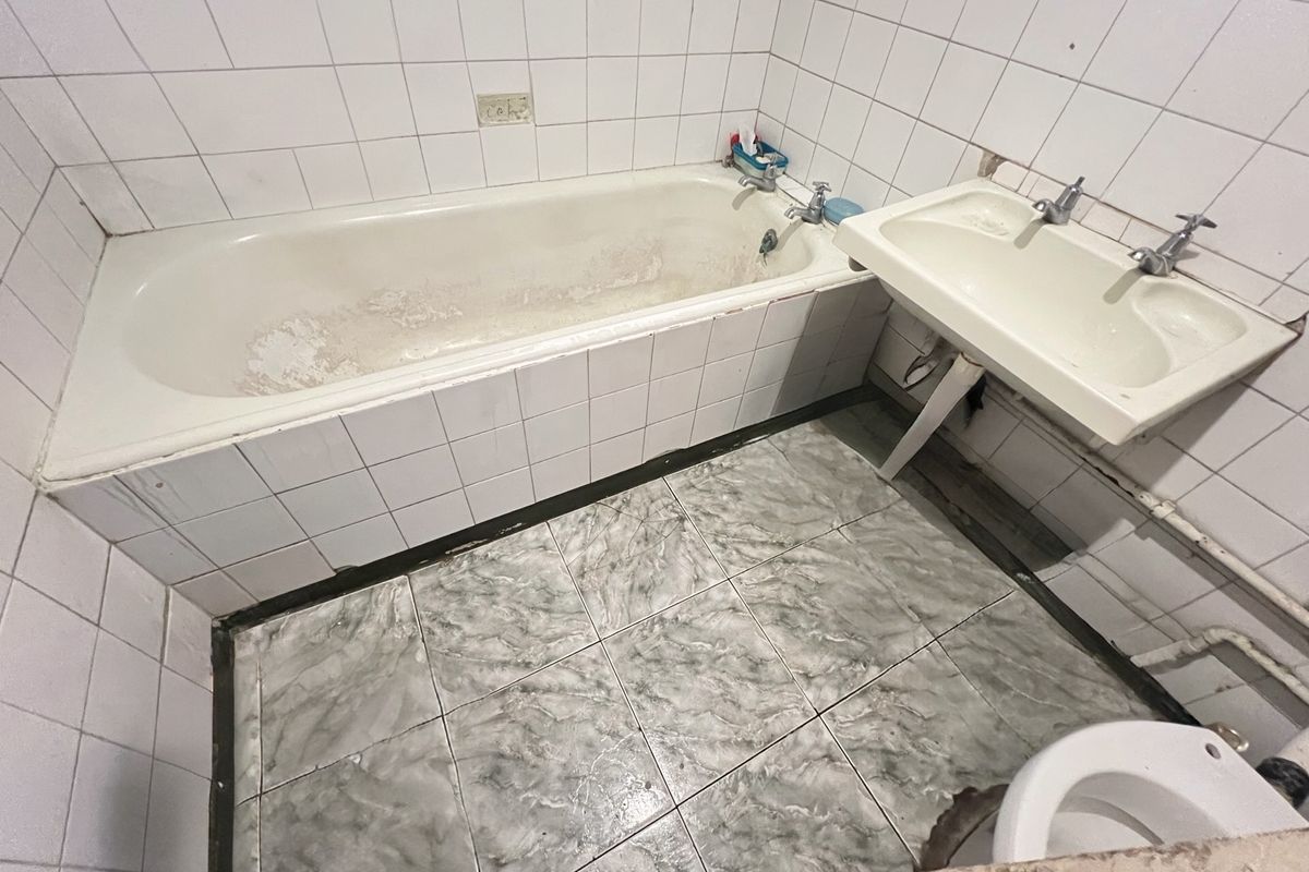 A dated bathroom featuring a worn bathtub, wall-mounted basin, and tiled finishes, requiring renovation to modernize the space.