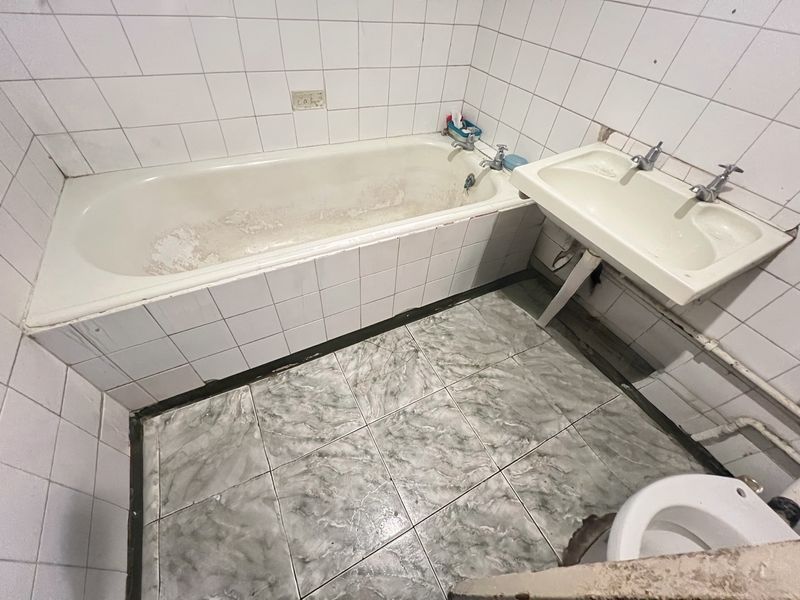 A dated bathroom featuring a worn bathtub, wall-mounted basin, and tiled finishes, requiring renovation to modernize the space.