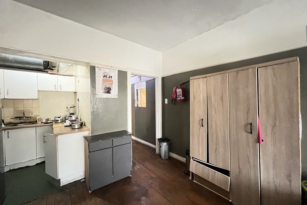 Open plan living area featuring timber flooring and an adjoining kitchen space with built-in cabinetry, requiring cosmetic updates and repairs.