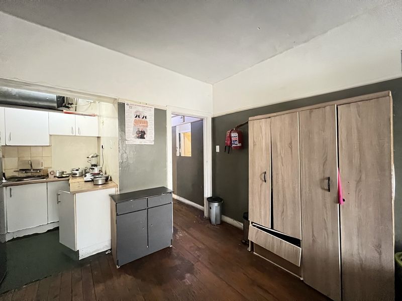 Open plan living area featuring timber flooring and an adjoining kitchen space with built-in cabinetry, requiring cosmetic updates and repairs.