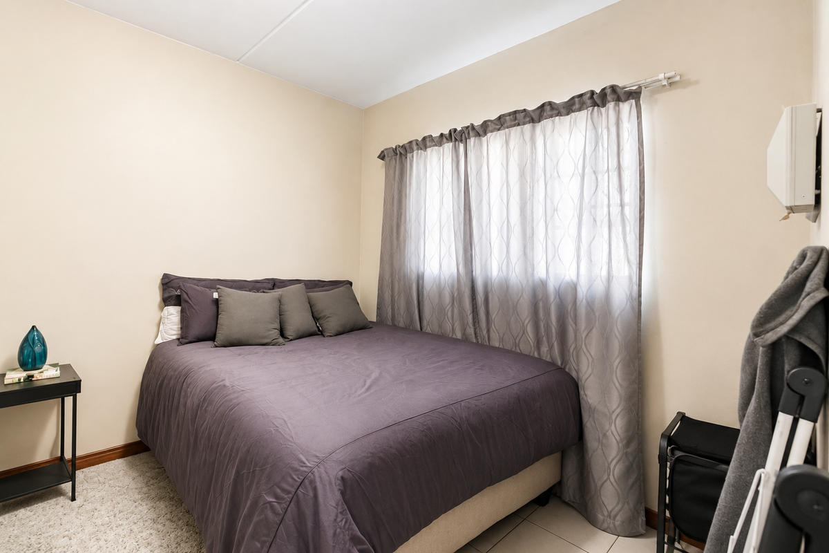 A compact bedroom featuring a mix of carpet and tile flooring, neutral wall tones, and a window fitted with a curtain rod.