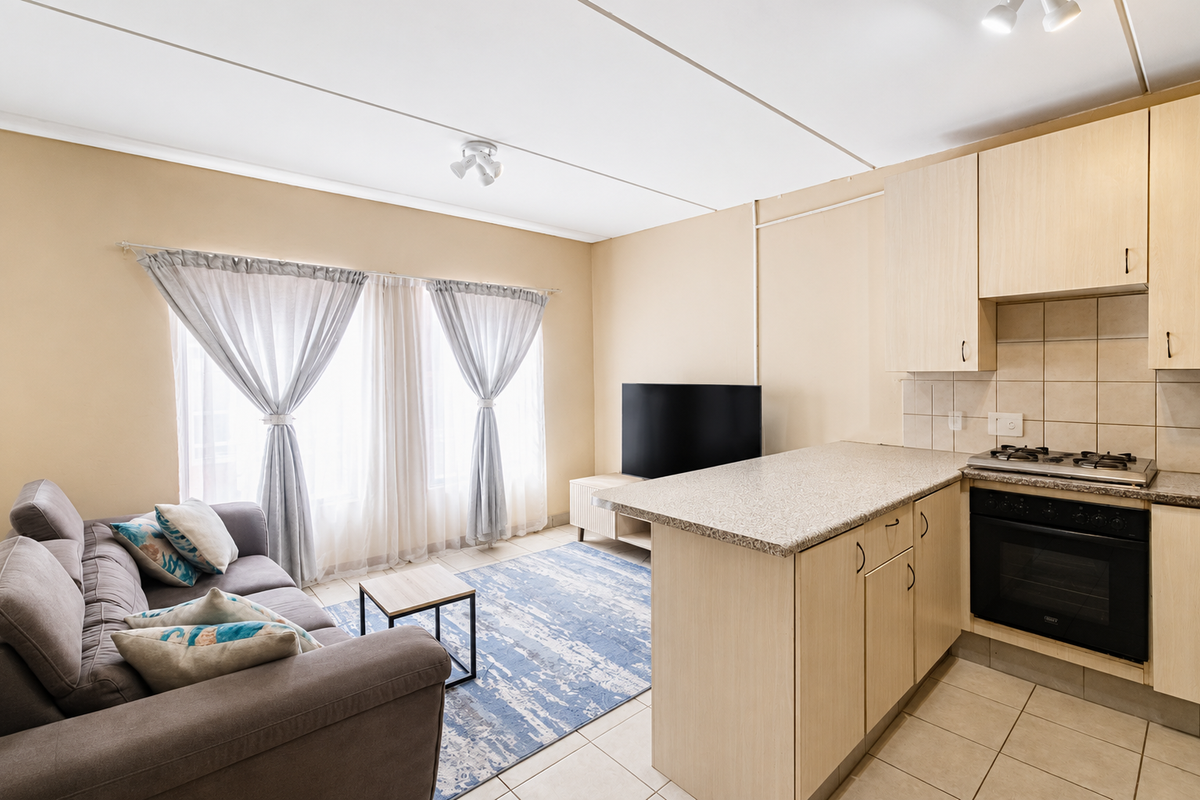 Open-plan living area featuring a functional kitchen with built-in cabinetry, gas hob, and oven, seamlessly flowing into a comfortable lounge space.