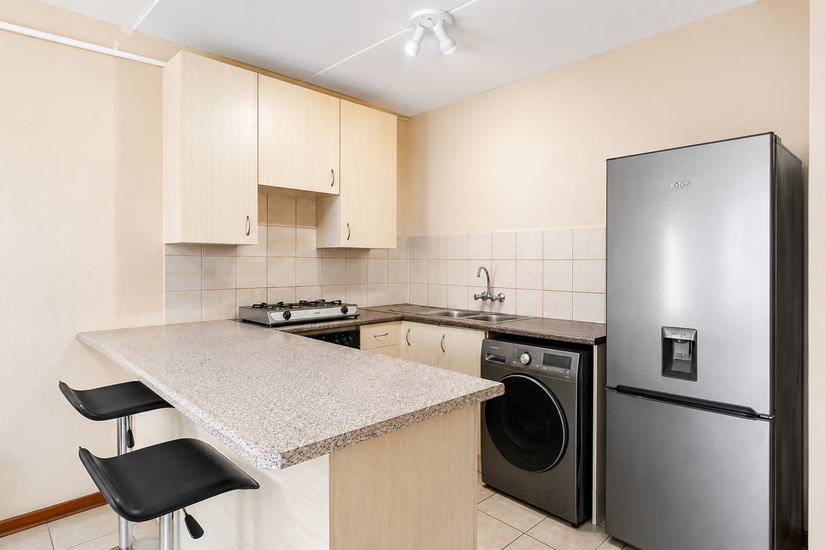 Compact kitchen featuring light wood-tone cabinetry, laminate countertops, a gas hob, double sink, and integrated laundry space with a breakfast bar.