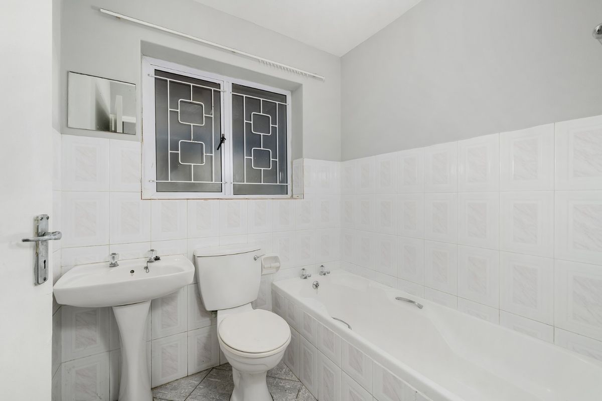 A functional bathroom featuring a pedestal basin, standard toilet, and a bathtub with tiled walls and security bars on the window.