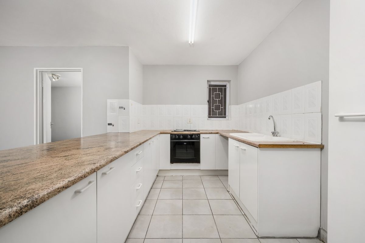 A functional kitchen featuring granite countertops, built-in oven, hob, and double basin sink with tiled backsplash and flooring.