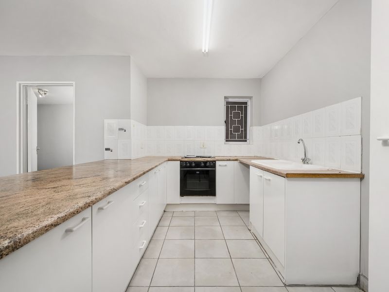 A functional kitchen featuring granite countertops, built-in oven, hob, and double basin sink with tiled backsplash and flooring.