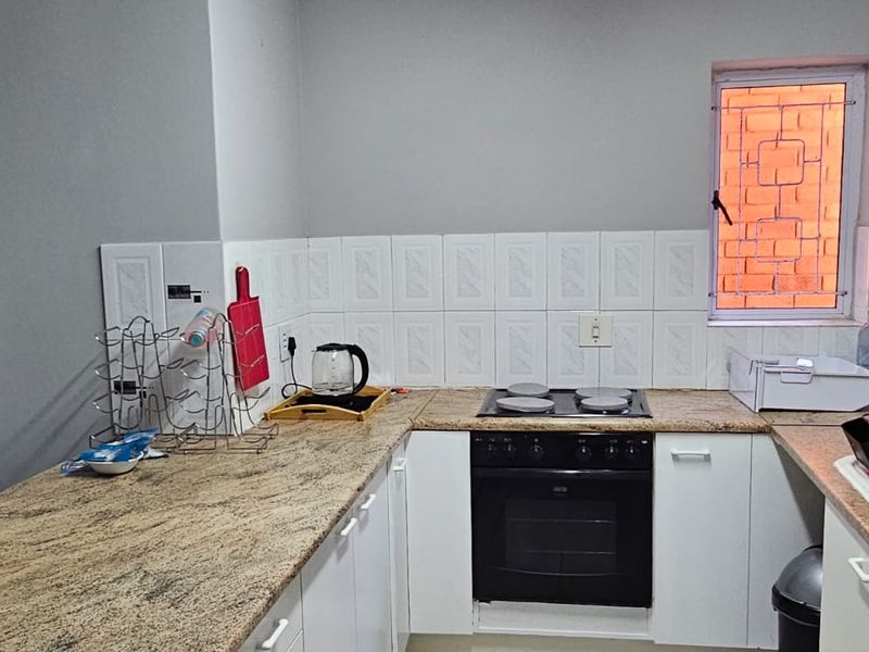 A functional kitchen featuring granite countertops, white cabinetry, a built-in oven with electric hob, and a tiled backsplash.