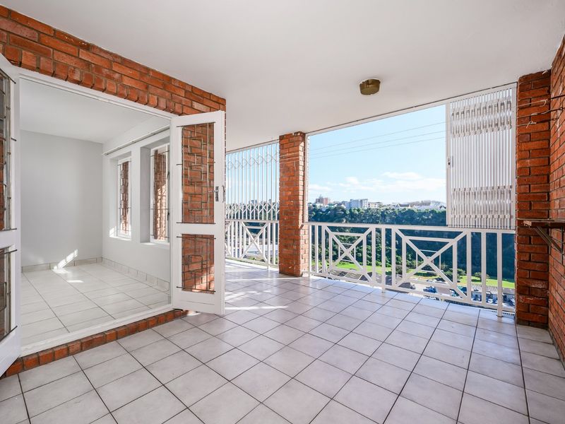 Spacious covered balcony featuring exposed brick walls, tiled flooring, and a metal balustrade, offering an open-air space with scenic views.