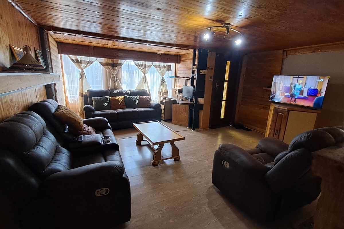 A cozy living room featuring extensive wood paneling on walls and ceiling, laminate flooring, and a built-in fireplace.
