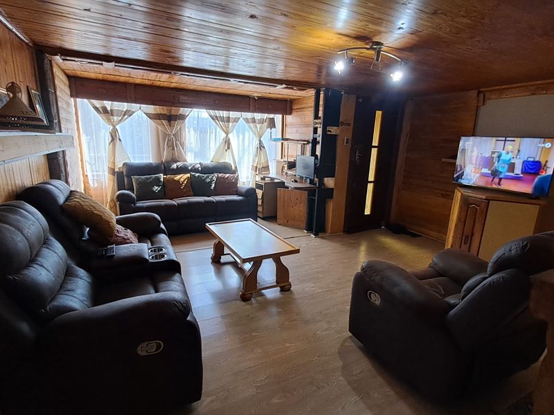 A cozy living room featuring extensive wood paneling on walls and ceiling, laminate flooring, and a built-in fireplace.