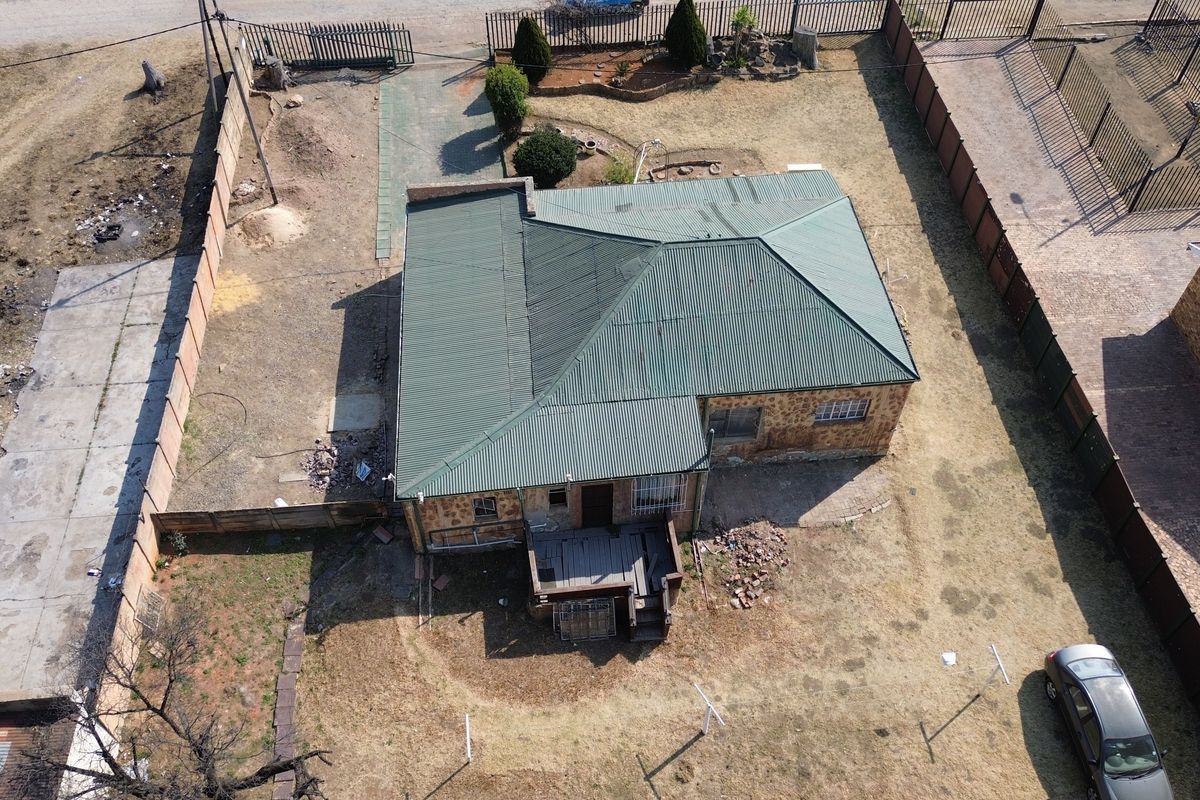 Aerial view of a detached house featuring a green corrugated metal roof, stone exterior walls, and a rear timber deck within a fenced plot.