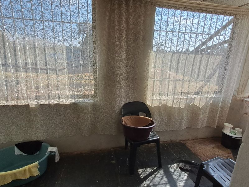 An enclosed patio or balcony area featuring security bars on the windows and worn flooring, offering a blank canvas for renovation.