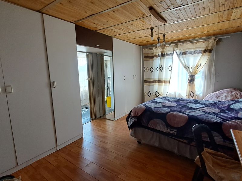 Bedroom featuring built-in cupboards, timber ceiling, and laminate flooring with access to an adjacent space via a sliding door.
