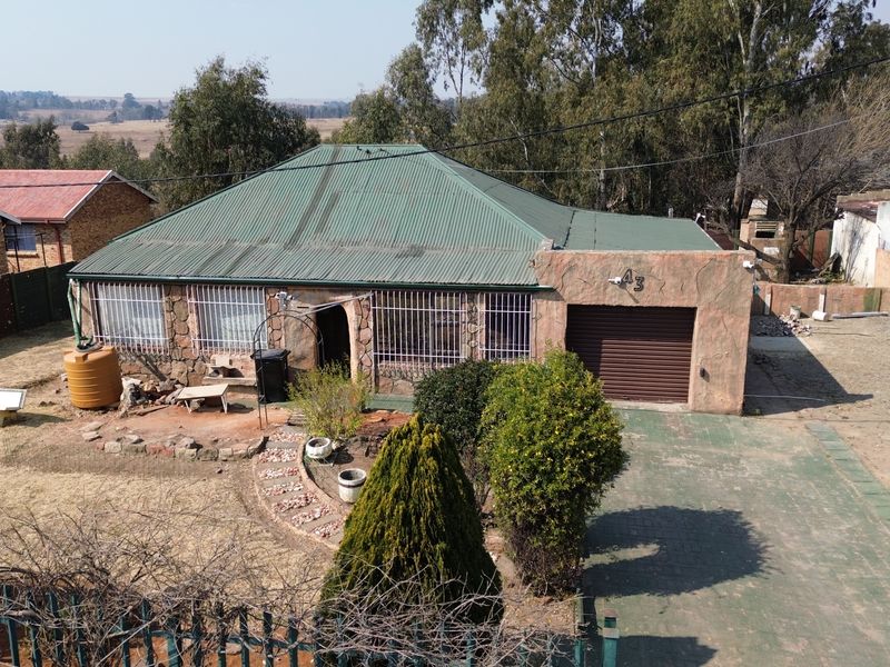Elevated view of a detached house featuring a corrugated metal roof, stone-clad facade, integrated roller shutter garage, and security bars on windows.