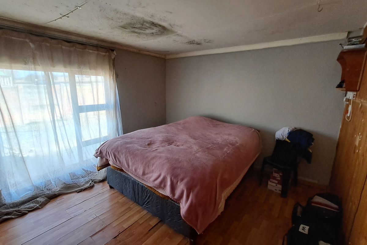 Bedroom featuring laminate flooring, timber wall paneling, and a sliding glass door, currently showing significant ceiling water damage and staining.