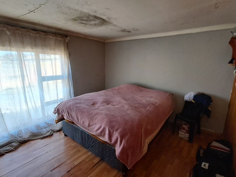 Bedroom featuring laminate flooring, timber wall paneling, and a sliding glass door, currently showing significant ceiling water damage and staining.