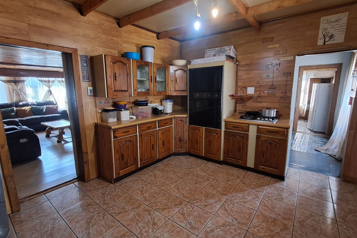 A rustic kitchen featuring wooden cabinetry, exposed ceiling beams, tiled flooring, and built-in cooking appliances, offering a traditional aesthetic with potential for modernization.