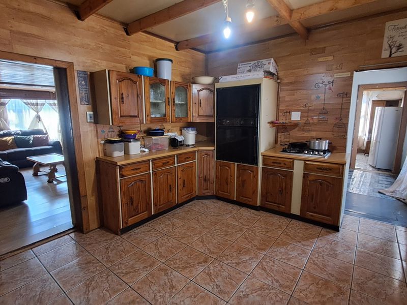 A rustic kitchen featuring wooden cabinetry, exposed ceiling beams, tiled flooring, and built-in cooking appliances, offering a traditional aesthetic with potential for modernization.
