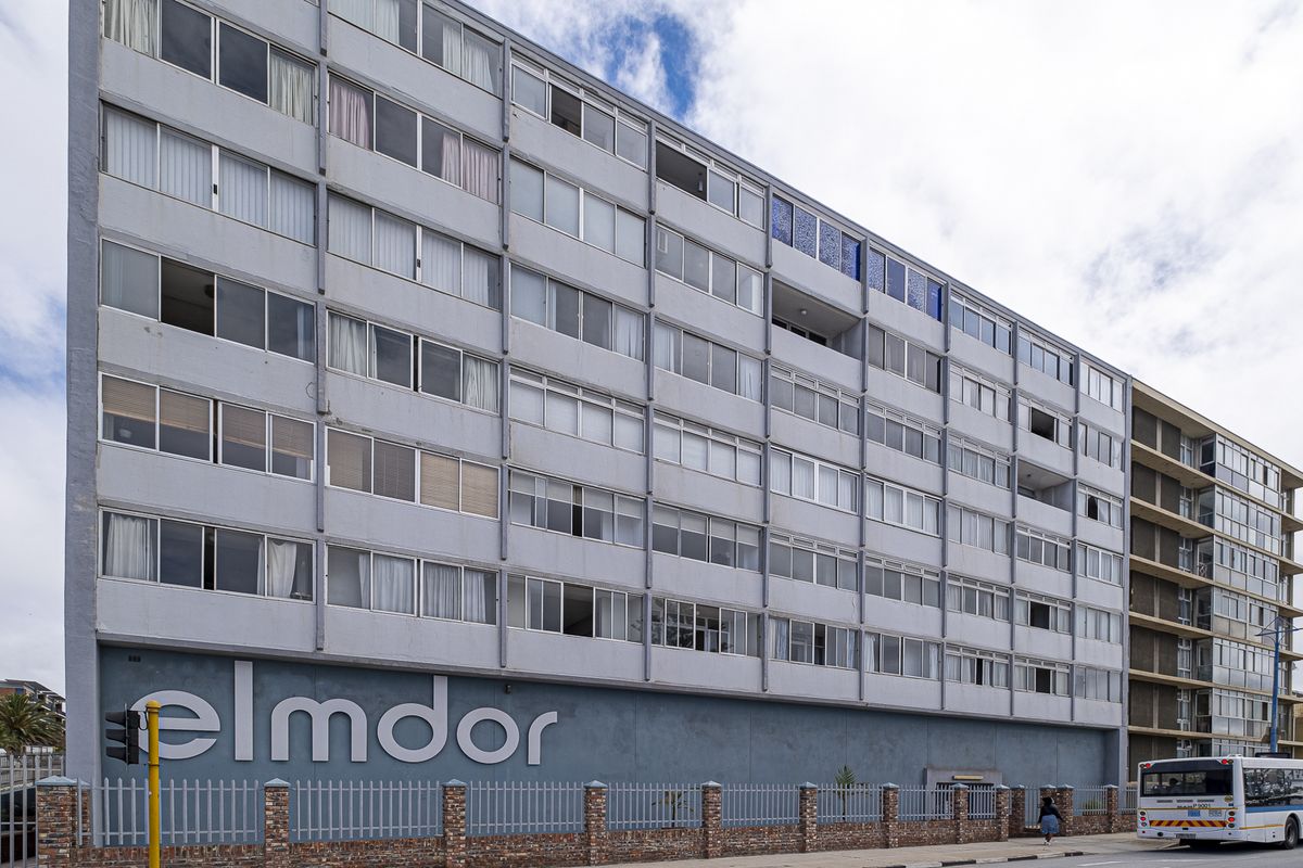 Street-facing view of the Elmdor apartment building, featuring a multi-story facade with large windows and a secure brick and metal boundary wall.
