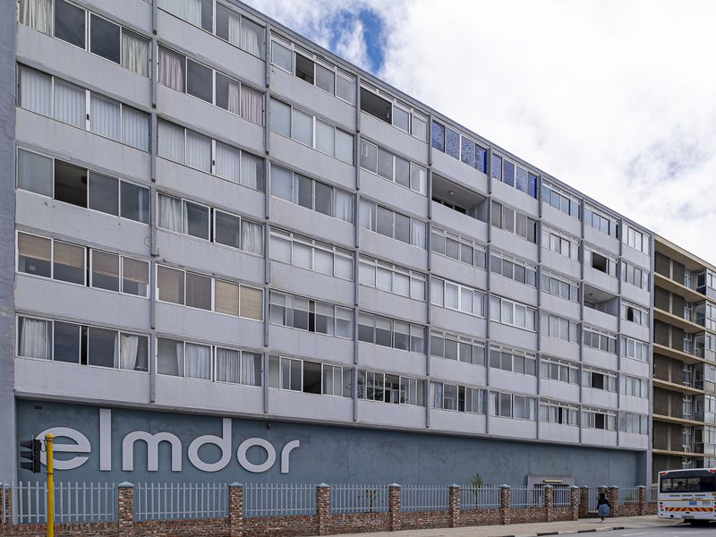 Street-facing view of the Elmdor apartment building, featuring a multi-story facade with large windows and a secure brick and metal boundary wall.