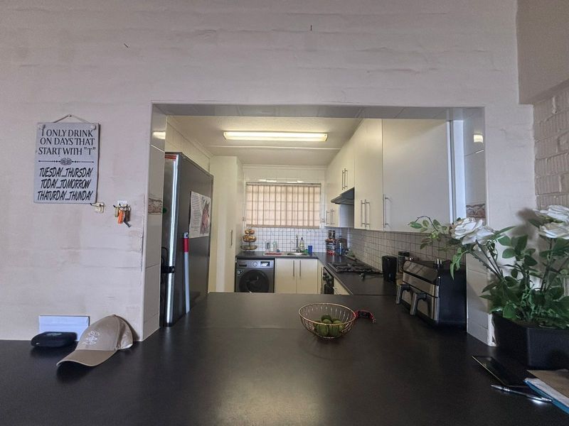 A functional kitchen featuring built-in cabinetry, dark countertops, a tiled backsplash, and integrated cooking appliances, viewed from an adjacent breakfast bar area.