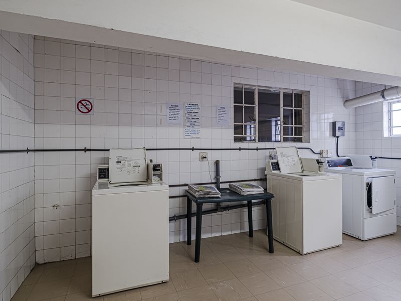 A functional communal laundry room featuring tiled walls, tiled flooring, and multiple washing machine and dryer connections.