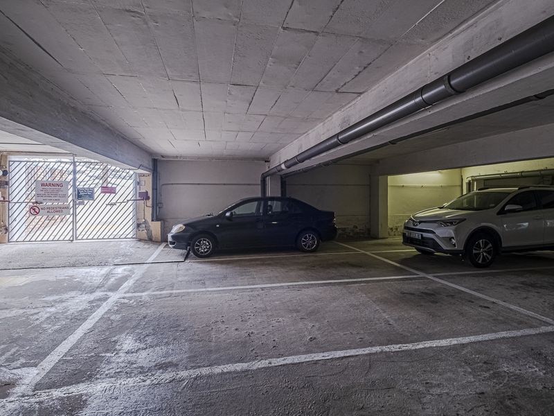 Underground parking garage featuring concrete flooring, exposed overhead piping, and a secure gated entrance.