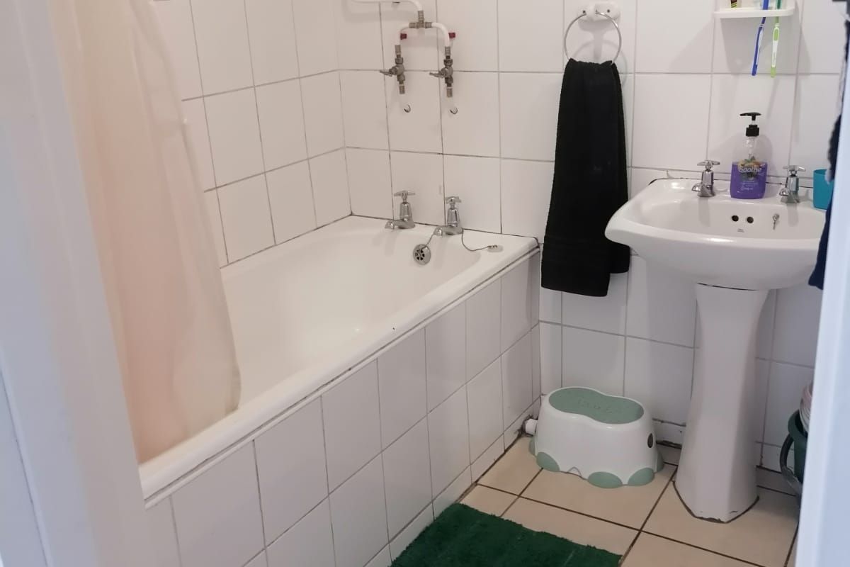 A functional bathroom featuring a pedestal washbasin, bathtub with shower mixer, and tiled finishes throughout, offering potential for modernization.