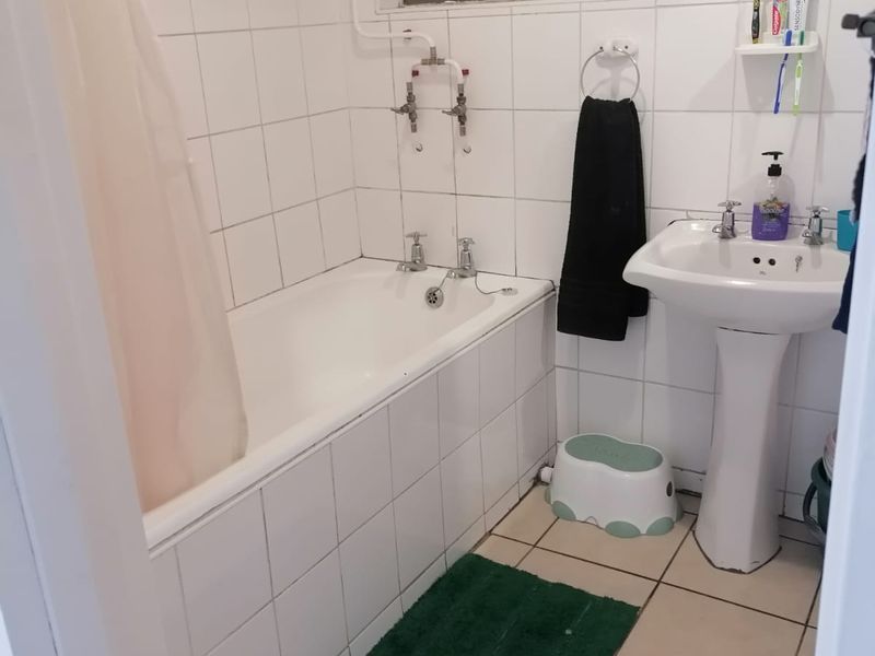 A functional bathroom featuring a pedestal washbasin, bathtub with shower mixer, and tiled finishes throughout, offering potential for modernization.