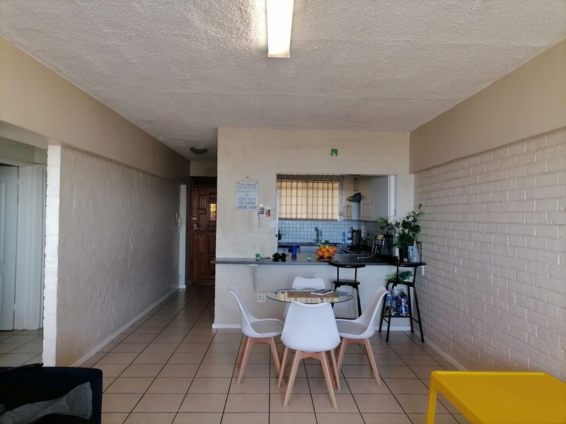 Open plan living and dining area featuring tiled floors, painted brick walls, and a convenient kitchen pass-through with a breakfast bar.