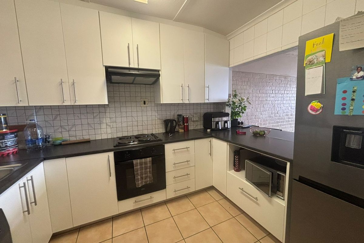 A functional kitchen featuring white cabinetry, dark countertops, a built-in oven and hob, tiled backsplash, and tiled flooring with a breakfast bar opening.