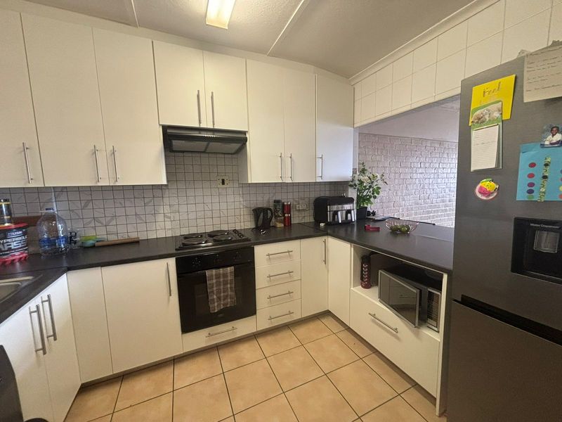 A functional kitchen featuring white cabinetry, dark countertops, a built-in oven and hob, tiled backsplash, and tiled flooring with a breakfast bar opening.