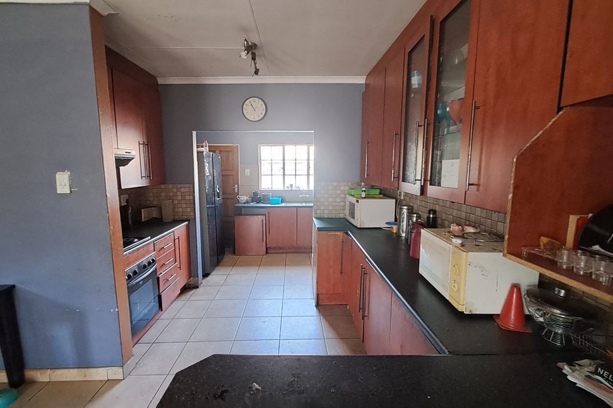 A functional kitchen featuring extensive wooden cabinetry, dark countertops, tiled flooring, and a dedicated prep area with a sink.