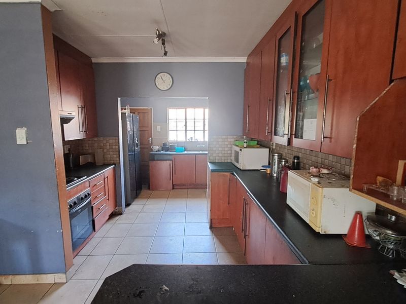 A functional kitchen featuring extensive wooden cabinetry, dark countertops, tiled flooring, and a dedicated prep area with a sink.