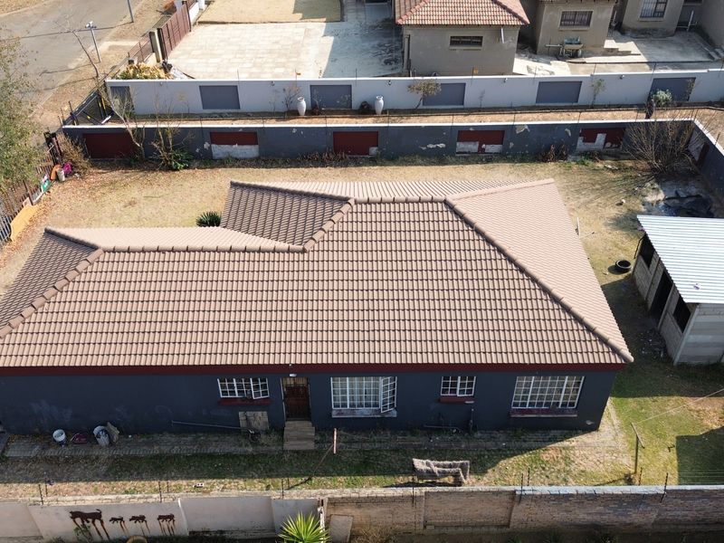 Aerial view of a residential property featuring a tiled roof, surrounding garden space, perimeter wall with security fencing, and a detached outbuilding.