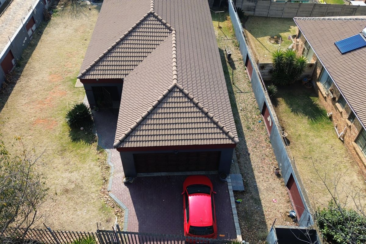 Aerial view of a residential property featuring a tiled roof, paved driveway, and surrounding boundary walls.